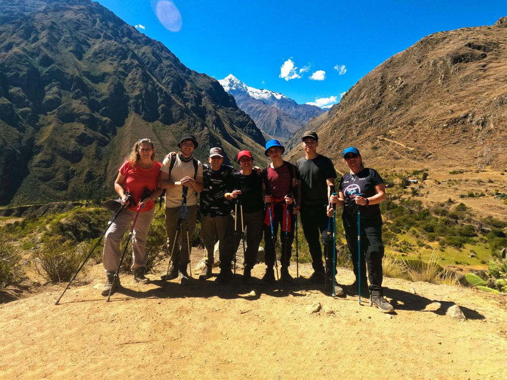 Group of hikers with trekking poles on the Classic Inca Trail with a snow-capped peak behind them