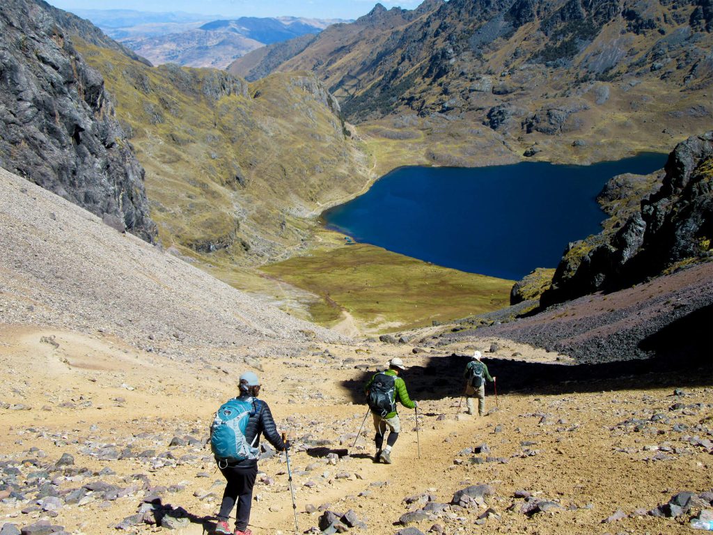 Inca Trail Sold Out? 2027 Alternatives Ranked by How Close They Feel 1 Hikers descending towards a deep blue glacial lake on the Lares trek