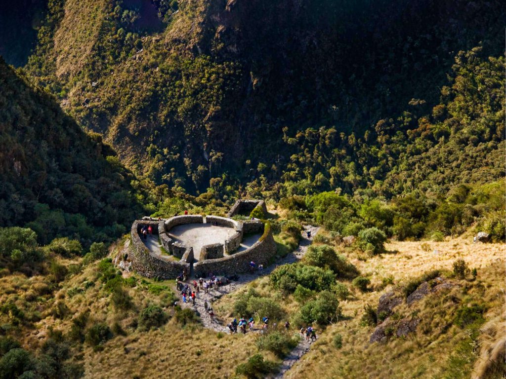 How Hard Is the Inca Trail? Altitude, Dead Woman’s Pass and How to Prepare 3 Hikers on the stone path approaching the circular Inca ruins of Runkurakay on the Inca Trail