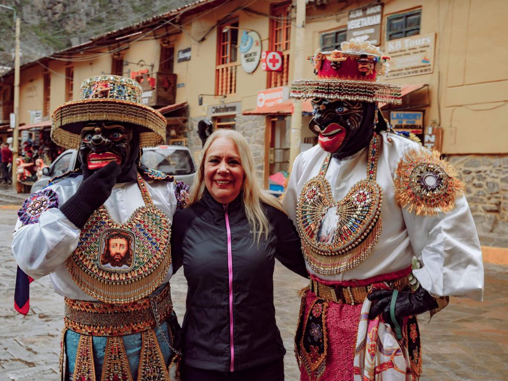 Planning the Inca Trail from the USA (2027): Passport, Flights, Time Zones and a 9-Day Plan 2 A traveler smiling between two masked dancers in colorful costumes in a Sacred Valley town