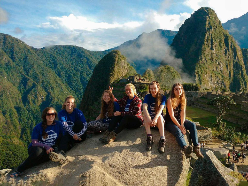 Planning the Inca Trail from the USA (2027): Passport, Flights, Time Zones and a 9-Day Plan 3 A group of hikers sitting on a rock at the classic Machu Picchu viewpoint with Huayna Picchu behind