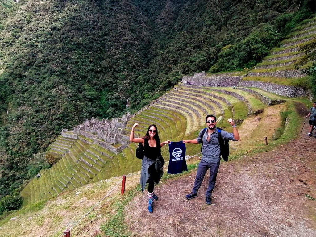 Two hikers holding a Terra Quechua t-shirt at the Wiñay Wayna terraces on the Inca Trail