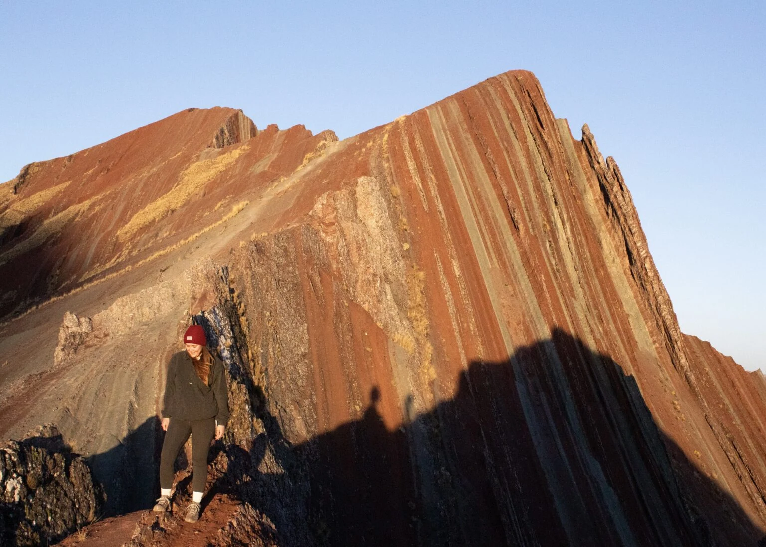 Hiker beside the red and ochre striped ridge of Pallay Punchu (Pallay Poncho), Cusco, in morning light