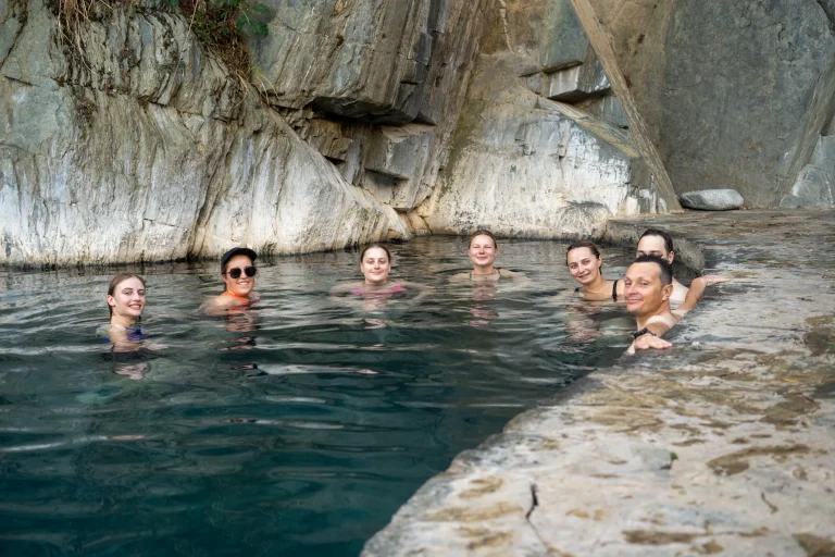 Hikers relaxing in the Cocalmayo hot springs pool beside a rock wall on the Inca Jungle trek