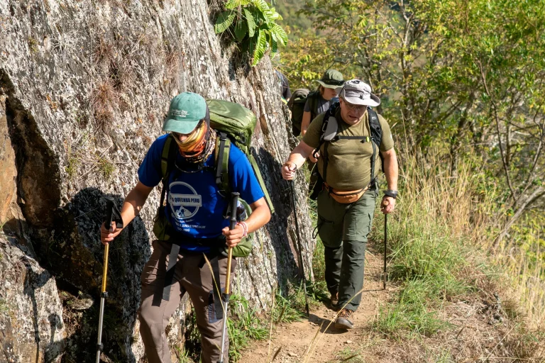 Terra Quechua guide and a hiker walking with trekking poles beside a rock wall on the Inca Jungle trek