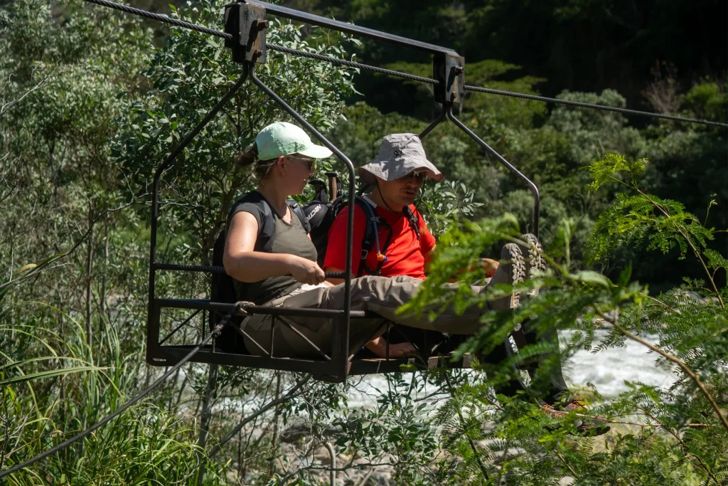 Dos viajeros cruzando el río en una oroya en la ruta Inca Jungle