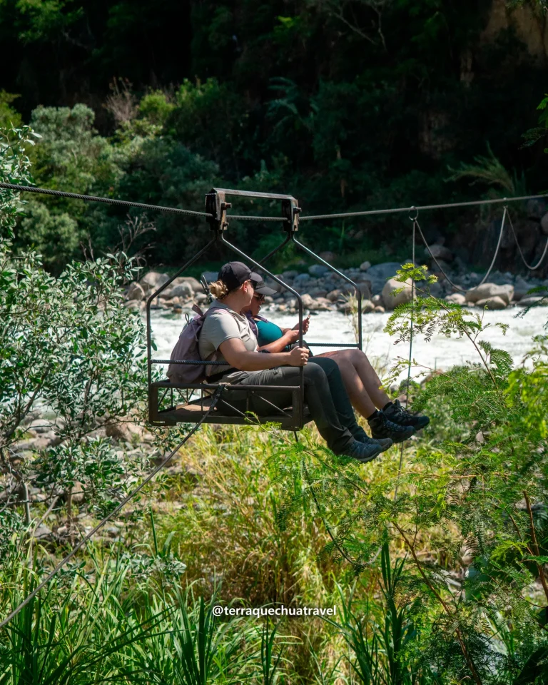 Two travelers crossing a river in a cable car basket (oroya) on the Inca Jungle trek