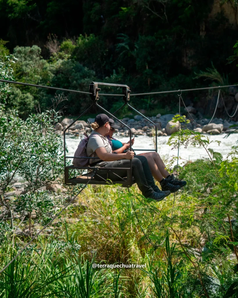 Two travelers crossing a river in a cable car basket (oroya) on the Inca Jungle trek