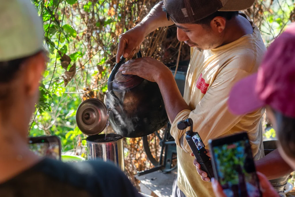 Farmer pouring freshly brewed coffee from a kettle while hikers take photos on the Inca Jungle trek
