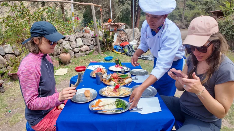 Chef in a white hat serving plates of food to hikers on the Lares trek