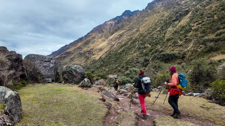 Two hikers walking a grassy trail through a rocky valley on the Lares trek