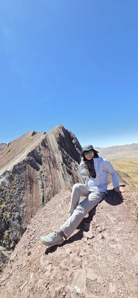 Hiker on the red ridge of Pallay Punchu with the red and green striped peak under a clear blue sky