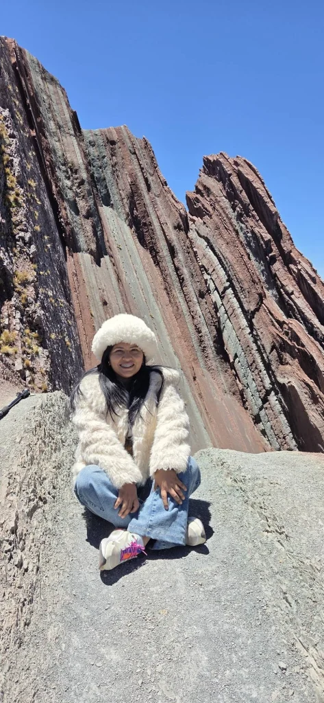 Traveler sitting in front of a red and green striped rock wall at Pallay Punchu