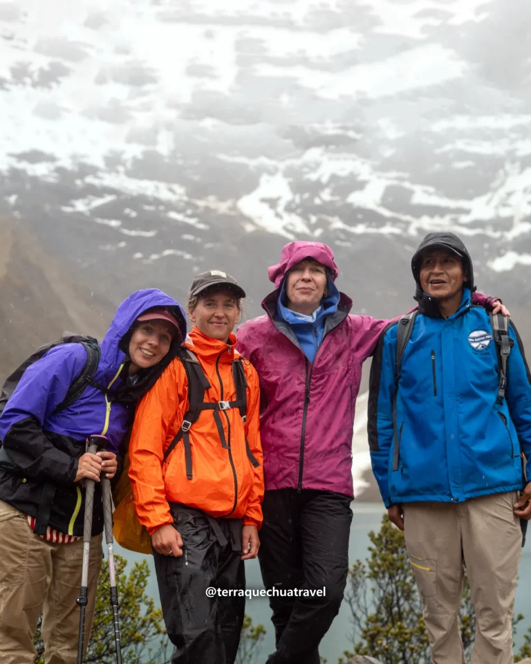 Guide and three hikers in rain gear smiling at Humantay Lake on the Salkantay trek