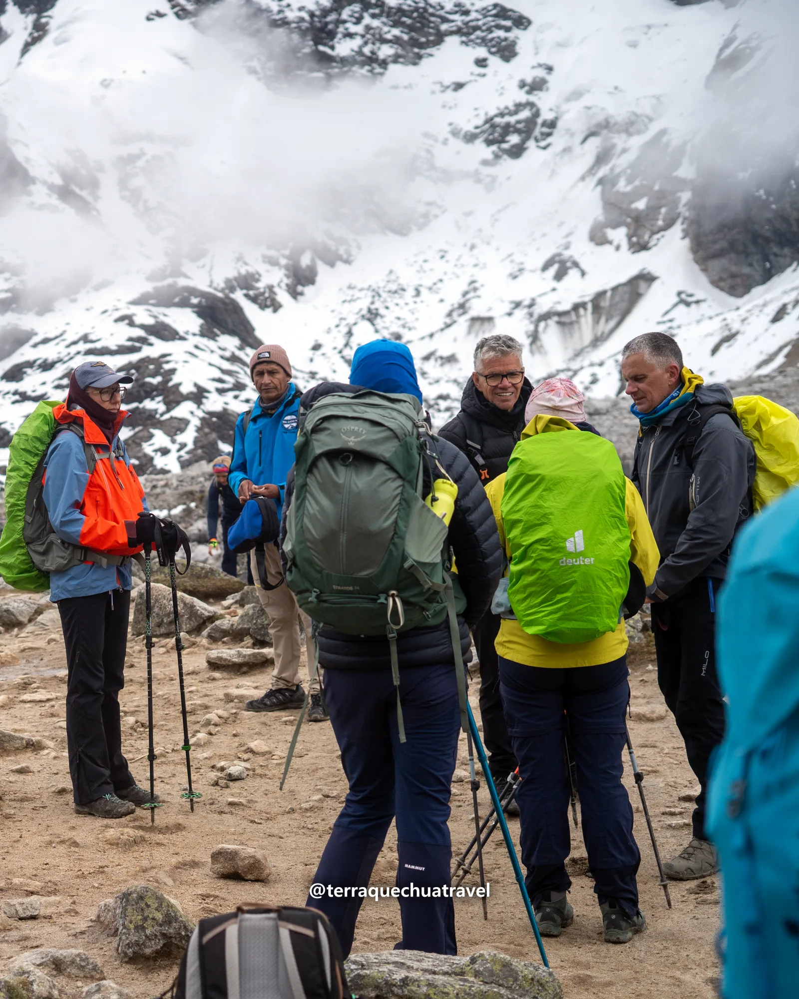 Group of hikers with backpacks and poles facing snow-covered peaks near the Salkantay pass