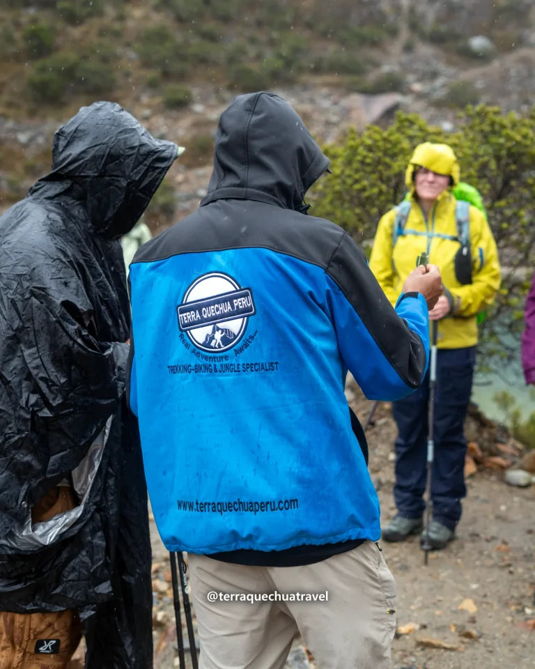Terra Quechua guide in a blue jacket talking with hikers in rain ponchos on the Salkantay trek